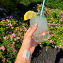 Hand holding a mason jar with lemon wedge and straw against a floral background