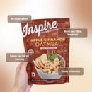 A hand holds a bag of Inspire Protein Kitchen Apple Cinnamon Oatmeal, featuring text highlights about its benefits, including no added sugar, being filling, and quick preparation for breakfast.