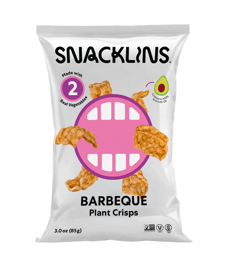 A bag of Snacklins Barbeque Plant Crisps features a playful design with a large pink mouth graphic, showcasing crispy snacks made from real vegetables and highlighting their avocado oil content.