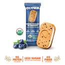 A pack of OLYRA Greek Yogurt Blueberry crème breakfast biscuits sits next to a biscuit filled with creamy yogurt and blueberries, highlighting its organic and nutritional benefits.