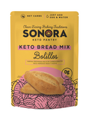 A yellow package of Sonora Keto Bread Mix features the product name prominently, with illustrations of bolillos and text highlighting low net carbs and preparation instructions.