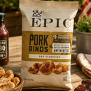 Bag of Epic Pork Rinds BBQ seasoning on a wooden table with a bottle of BBQ sauce.