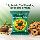 A vibrant green bag of Crisp Power Protein Pretzels displays a pretzel snack, highlighting 28 grams of protein and 6 net carbs, with a bowl of mixed seeds nearby and additional pretzels in the background.