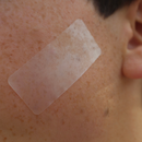 A close-up of a person's skin with a translucent rectangular pimple patch strip applied to the cheek.