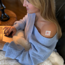 Woman wearing a light blue sweater with a visible tattoo on her arm, sitting indoors.