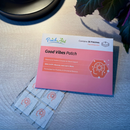 A pink package labeled "Good Vibes Patch" sits on a light wooden surface with several small patches featuring a brain icon, promoting mood support with botanical ingredients.