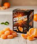 A box of "Gym Candy Bursts" in Swole Citrus flavor sits on a wooden surface, surrounded by orange gummies and fresh citrus slices, highlighting the product's vibrant color and fruity appeal.
