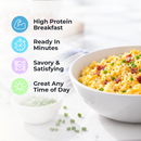 A bowl of fluffy scrambled eggs topped with green onions and bacon bits sits on a light surface, accompanied by a small bowl of chopped chives, highlighting a high-protein breakfast option.