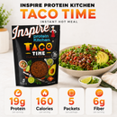 Package of Inspire Protein Kitchen Taco Time Instant Hot Meal displayed beside a bowl of taco filling topped with avocado and greens, with a small bowl of lime wedges nearby.