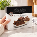 Woman holding a box of Inspire Low Carb Protein Fiber Bars – Chocolate Crisp in a kitchen.