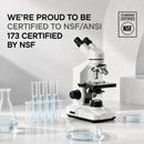 A white microscope is prominently displayed beside a rack of four test tubes with blue liquid, featuring text about NSF/ANSI certification in a modern, well-lit laboratory setting.