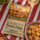 Packaging of barbecue protein crisps on a red and white striped tablecloth with a bowl of crisps beside it.