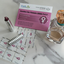 A pink package labeled "Awaken Her Female Libido Patch" sits on a marble surface alongside a silver lipstick, a roll of patches, and a perfume bottle, suggesting a focus on enhancing female libido and well-being.