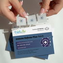 A hand holds a transparent packet containing three health patches while a product box labeled "Immune Defense Plus Patch" with details about its benefits and ingredients is visible beneath.