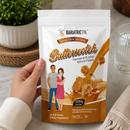 A hand holds a stand-up pouch of BariatricPal Butterscotch soft chew dietary supplement. The white and brown package features illustrations of a man and woman and a butterscotch splash graphic.