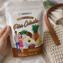 A hand holds a white stand-up pouch of BariatricPal Pina Colada calcium citrate soft chews. The packaging features illustrations of pineapples, a pineapple slice, a couple, and a brown gradient base.