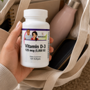 A hand holds a white bottle of BariatricPal Vitamin D-3 softgels in front of an open beige tote bag containing other items.