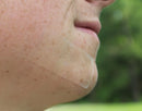 A close-up of a person's cheek and jawline with a transparent rectangular pimple patch strip applied to the skin.