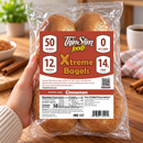 A hand holds a clear bag of ThinSlim Foods Xtreme Cinnamon Bagels, displaying nutritional information highlighting 50 calories, 12g protein, and 0 net carbs, with a cozy kitchen setting in the background.