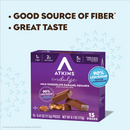 A purple box of Atkins Endulge Milk Chocolate Caramel Squares displays nutritional highlights, including low sugar and high fiber, with pieces of chocolate shown in front against a light blue background.