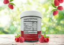 A white container with a nutrition label is surrounded by fresh raspberries on a marble surface, set against a blurred green background, suggesting a fruity dietary supplement.