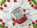 A clear container of dietary supplement gummies with a white lid displays the nutrition label, surrounded by fresh raspberries and mint leaves on a marble surface.
