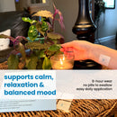 A hand reaches towards a lit candle while resting on a table with a plant and product packaging, showcasing a calming patch that supports relaxation and balanced mood.