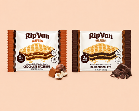 Two packages of RipVan Wafers, one labeled "Chocolate Hazelnut" and the other "Dark Chocolate," are displayed against a light peach background, with hazelnuts and chocolate pieces beside each package.