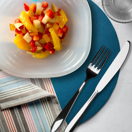 A bowl of colorful fruit salad, including orange, red pepper, and apple pieces, is placed on a blue placemat alongside a fork, knife, and a striped napkin.