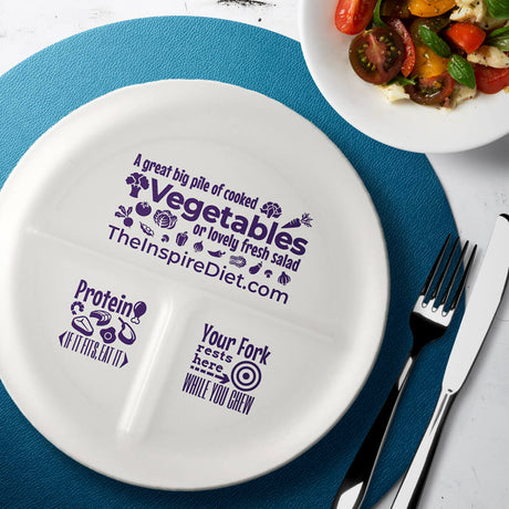 A divided white plate with purple text promotes healthy eating, featuring sections labeled for vegetables, protein, and a reminder for fork placement while eating, set on a blue placemat next to a bowl of salad.